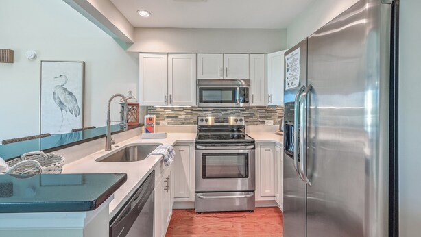 A modern kitchen with stainless steel appliances, white cabinets, and a tiled backsplash. - 2942 Atrium Villa (Seabrook Island)