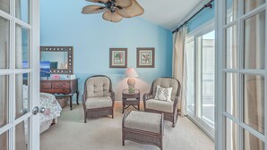 A room with a ceiling fan, two armchairs, a small table with a lamp, a mirror, and framed pictures on the wall. - 2942 Atrium Villa (Seabrook Island)