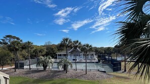 A beachfront property with a large house, a tennis court, and a fenced area with palm trees. - 2942 Atrium Villa (Seabrook Island)