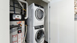 Ein kleiner Waschraum mit einer Frontlader-Waschmaschine und -Trockner, einem Warmwasserbereiter und freiliegenden Wasserleitungen.