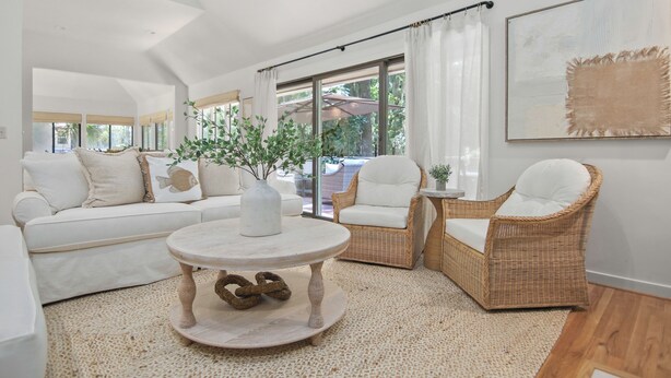 A modern living room with a white sofa, wicker chairs, a round coffee table, and a large window with curtains. - 2908 Captain Sams (Seabrook Island)