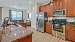 A modern kitchen with granite countertops, stainless steel appliances, and wooden cabinets. - 261 Lasso Drive 6bed (Kissimmee)