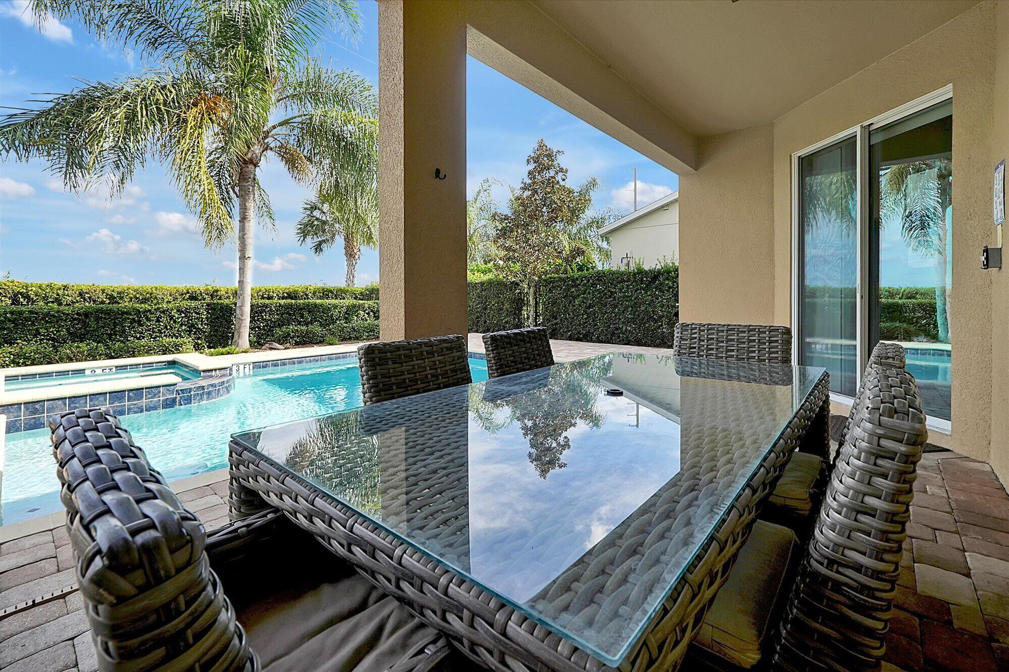 A glass-top table with wicker chairs, a pool, and a view of the surrounding greenery.