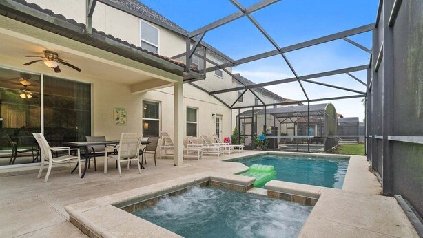 A covered outdoor swimming pool area with a hot tub, lounge chairs, and a patio table. - 2820-5-rc-impeccable Corner lot Home (Kissimmee)