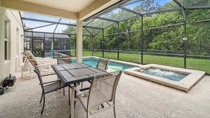 A covered patio with a pool and hot tub, surrounded by glass walls and a view of a lush garden. - 2820-5-rc-impeccable Corner lot Home (Kissimmee)