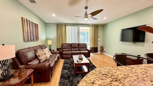 A living room with a brown leather sofa, a coffee table, a TV, and a ceiling fan. - 2820-5-rc-impeccable Corner lot Home (Kissimmee)
