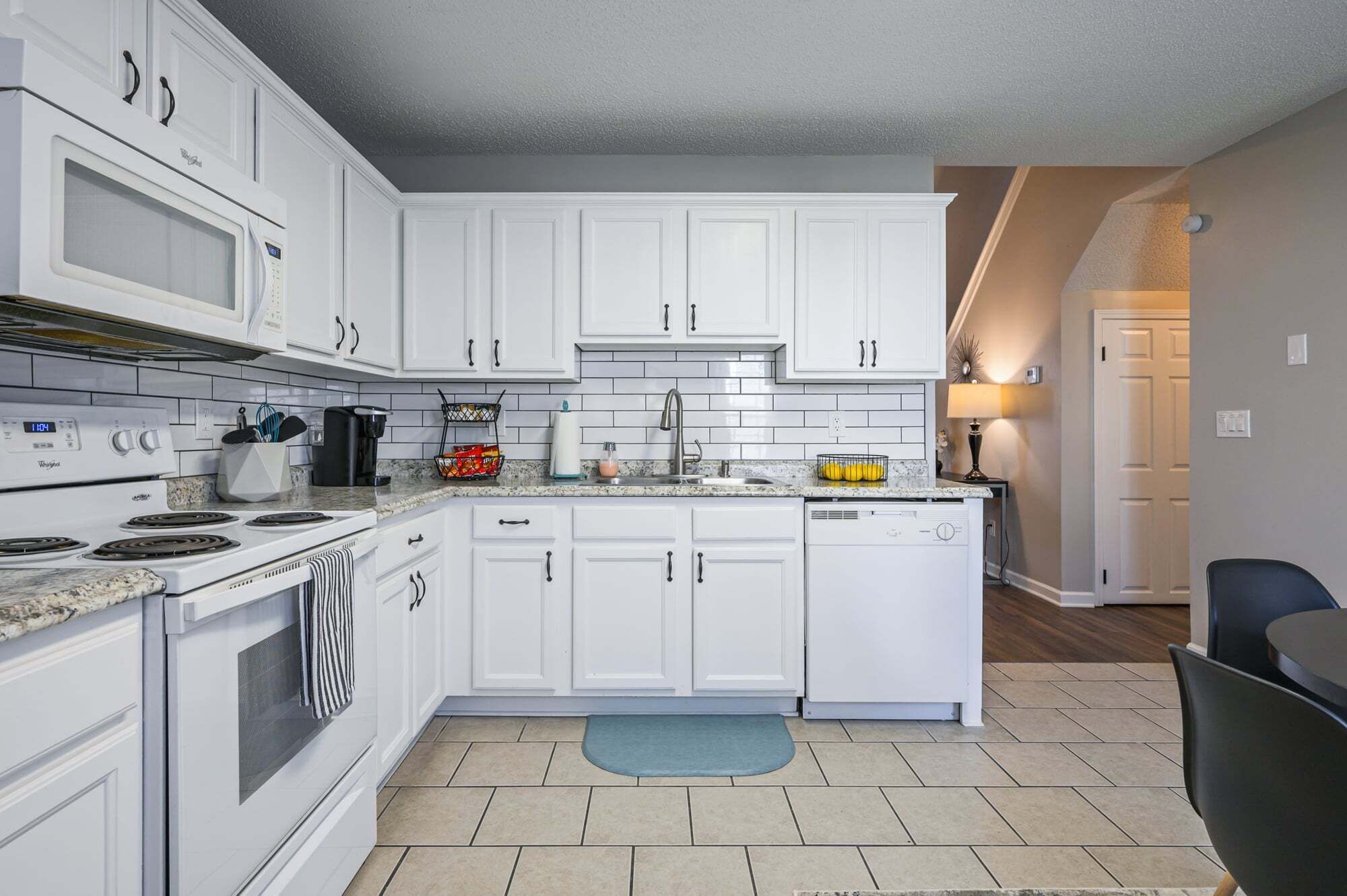 A kitchen with white cabinets, a microwave, stove, and dishwasher. There is a countertop with a coffee maker, a fruit basket, and a sink.
