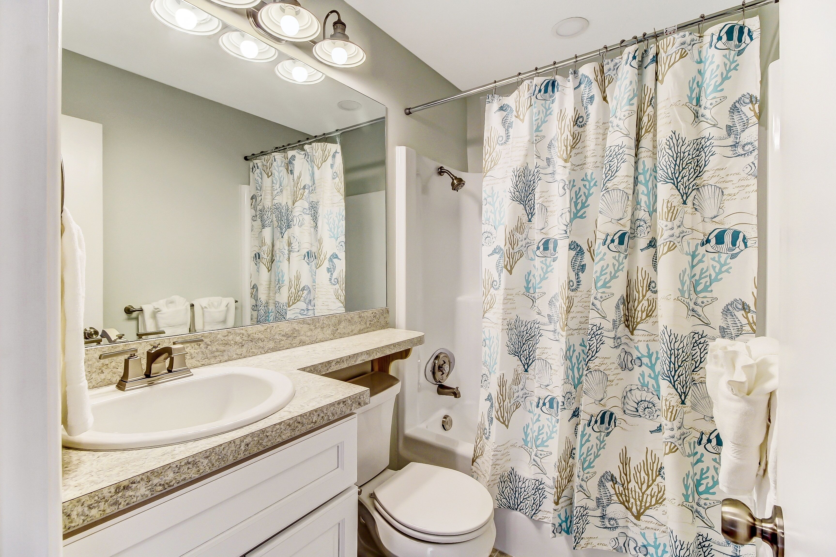 Une salle de bain équipée d’un lavabo, d’un miroir, de toilettes et d’un rideau de douche orné de motifs représentant la vie marine.