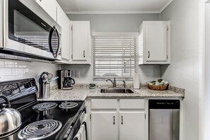 Una cocina moderna con armarios blancos, estufa de acero inoxidable, microondas, lavavajillas y una ventana con persianas.