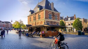 A historic building with a prominent clock tower, surrounded by a cobblestone square with outdoor seating and bicycles. - Boerderijkamer Eeltjesmar bij Leeuwarden (Weidum)