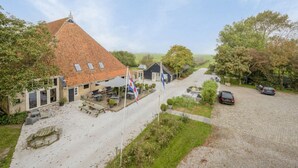 A rural building with a tiled roof, outdoor seating, and a gravel driveway. - Boerderijkamer Eeltjesmar bij Leeuwarden (Weidum)