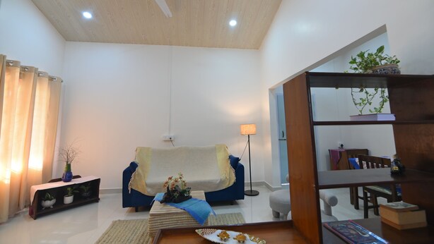 A living room with a ceiling fan, a sofa, a floor lamp, a bookshelf, and a potted plant. - Rün Lirak, Lovely Home: Tremendous 2-bedroom house with AC in Guwahati (Guwahati)