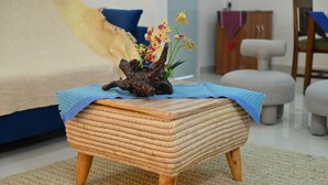 A woven stool with a decorative piece on top, placed on a textured rug in a room with a sofa and a chair. - Rün Lirak, Lovely Home: Tremendous 2-bedroom house with AC in Guwahati (Guwahati)