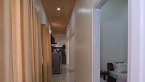 A hallway with a wooden ceiling, beige curtains, a bed with a patterned blanket, and a small table. - Rün Lirak, Lovely Home: Tremendous 2-bedroom house with AC in Guwahati (Guwahati)
