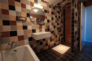 Ein Badezimmer mit Wand aus Schachbrettfliesen, einem Waschbecken, einem Spiegel, einer Dusche und einer Tür zu einem anderen Raum.