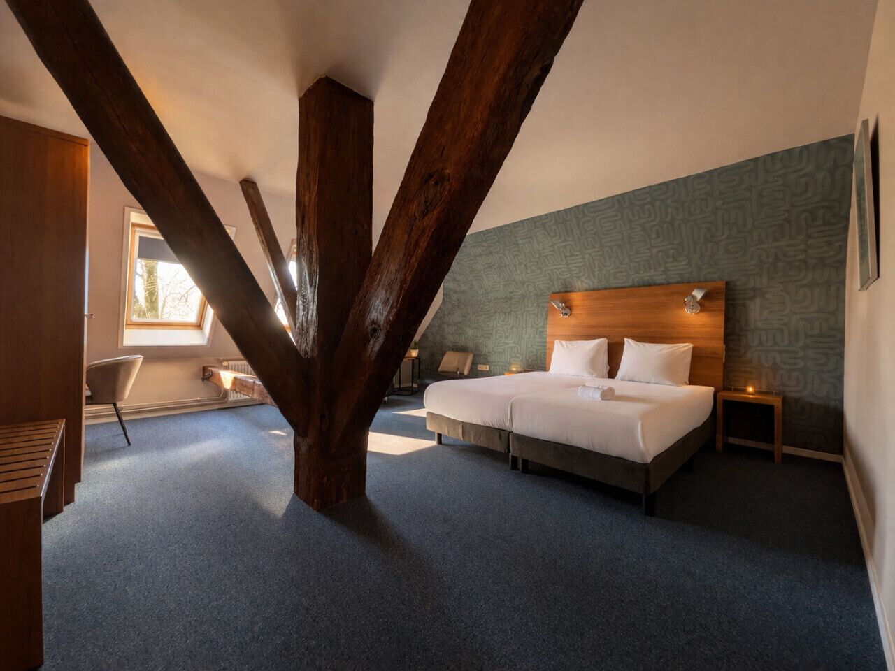 A bedroom with a large bed, a wooden ceiling beam, a nightstand, and a window.