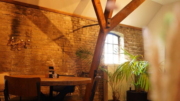 Un comedor rústico con pared de ladrillo, vigas de madera y una mesa redonda con sillas.