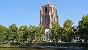 Una torre histórica con un reloj, rodeada de árboles y una masa de agua.