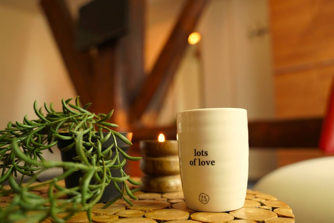 Eine Kerze, eine Tasse mit dem Aufdruck „lots of love“ und ein Rosmarinzweig auf einem runden Tisch.