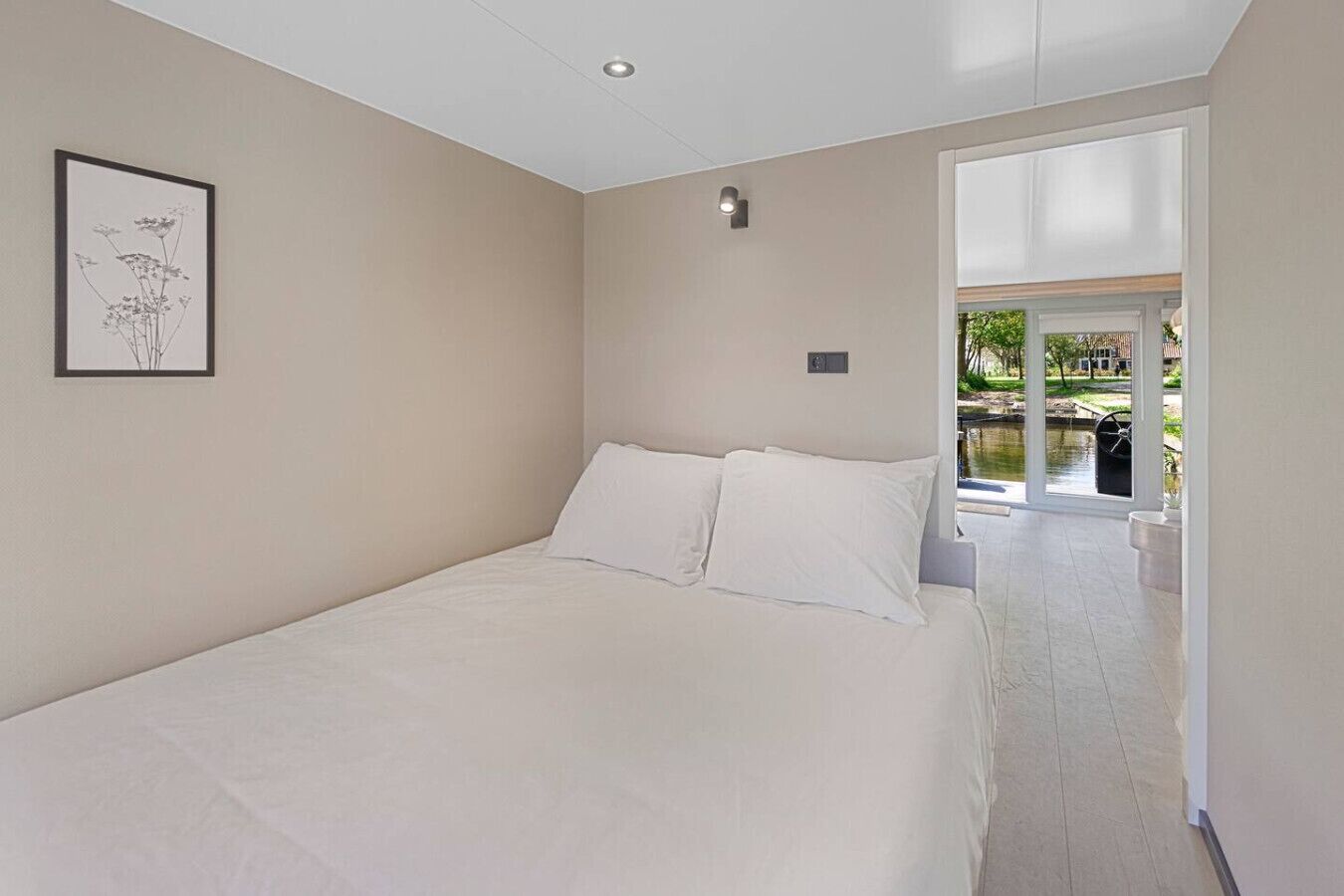 A bedroom with a large bed, a framed picture on the wall, and a view of a garden through a sliding door.