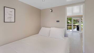 A bedroom with a large bed, a framed picture on the wall, and a view of a garden through a sliding door.