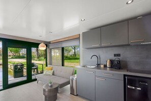 Una cocina moderna con armarios grises, un fregadero y una cafetera. Hay un sofá y una mesita con una planta.