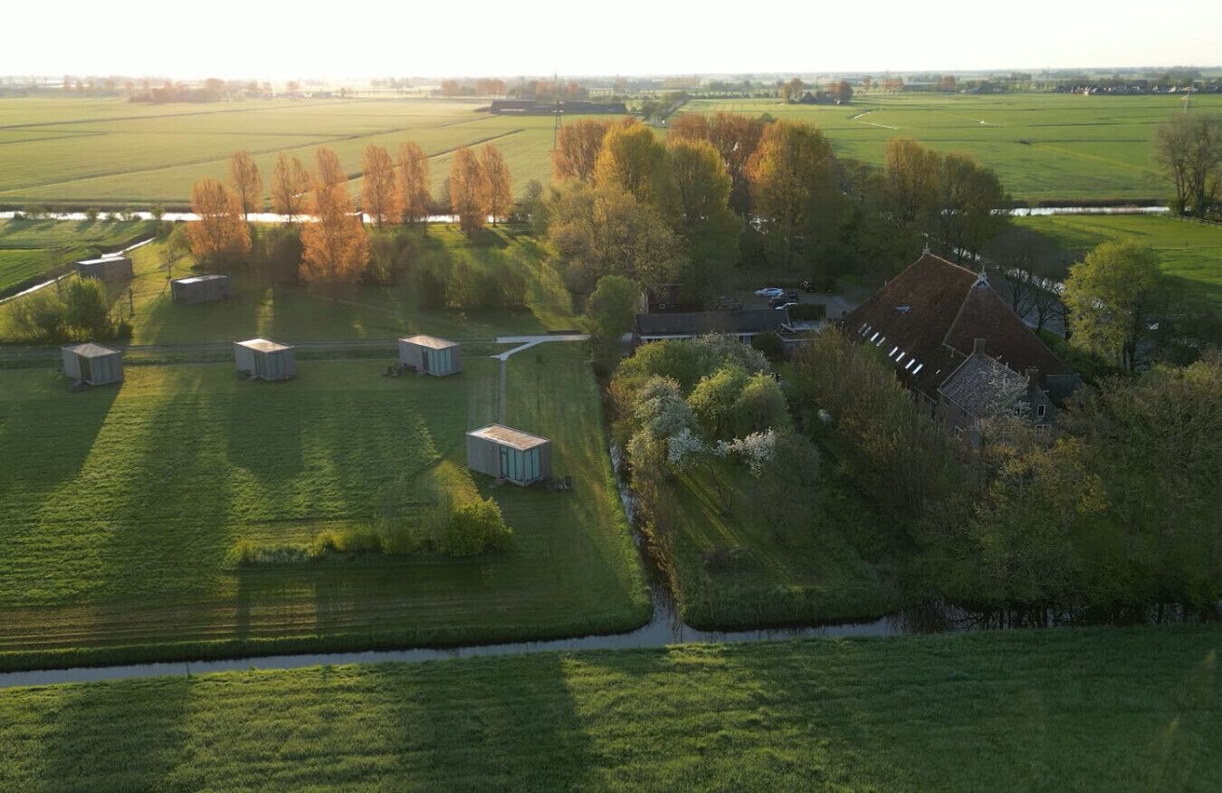 Vue aérienne d’une propriété rurale comprenant plusieurs petits bâtiments, une grande maison et de vastes champs verdoyants.