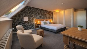 Een slaapkamer met een schuine balkenlaag, een bed, een stoel, een tafel en een muur met een bloemendesign.