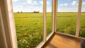 Een kamer met een groot raam met uitzicht op een groen veld en een heldere lucht.