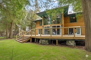 A wooden house with a deck, large windows, and a staircase leading to the entrance.