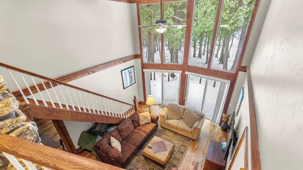 Un espace de vie à plusieurs niveaux, avec un escalier en bois, un canapé en cuir marron et une vue sur un espace extérieur enneigé, grâce à de grandes fenêtres.