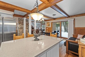 A spacious kitchen with a large island, wooden beams, stone walls, and a view of the outdoors.