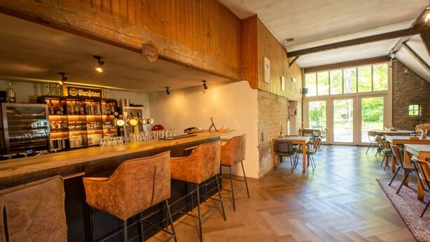 Una zona de bar con taburetes, una barra y un letrero que dice 'Wurstinger'. Hay mesas y sillas en el área de comedor contigua.