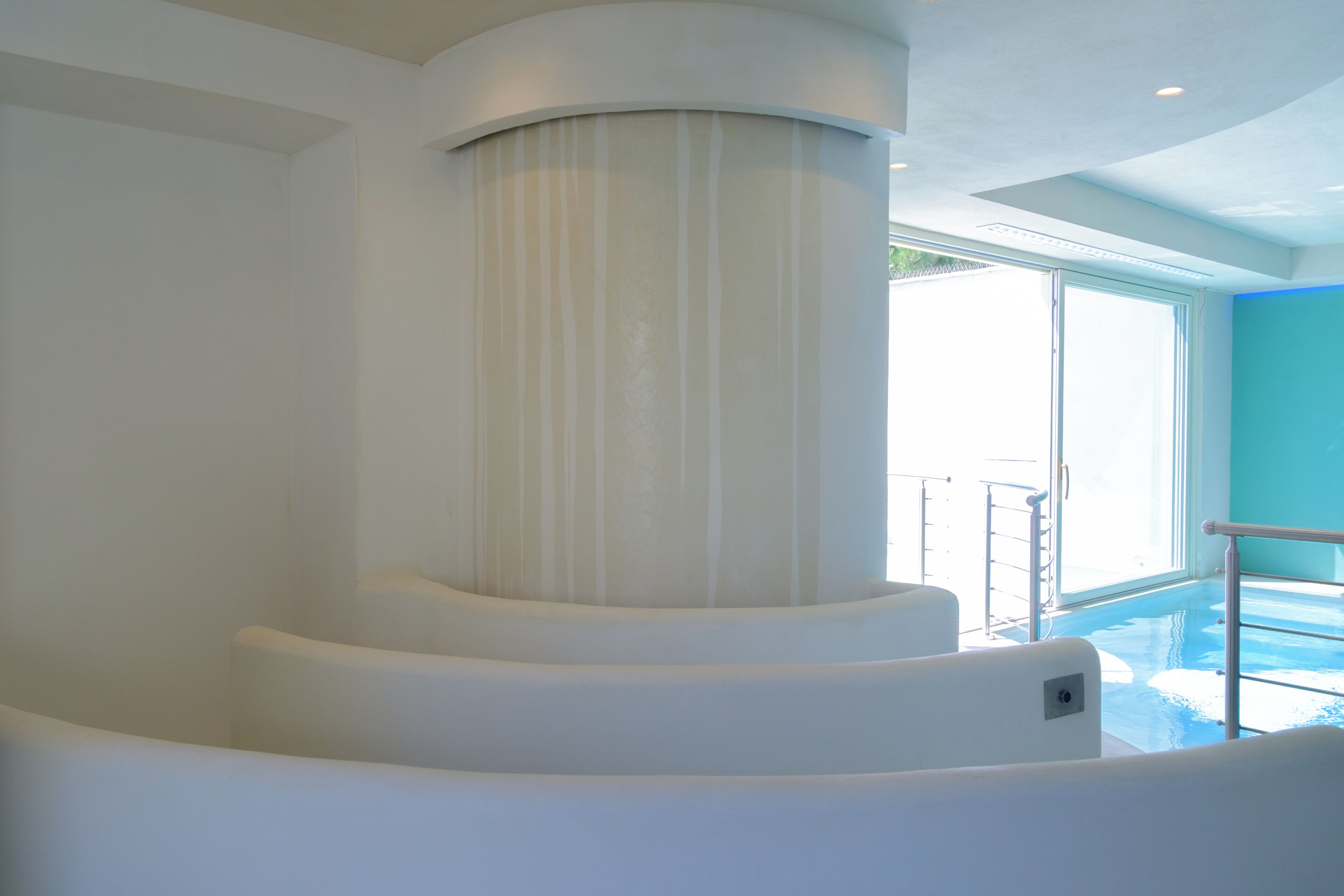 Un intérieur moderne avec une structure blanche aux lignes courbes, une porte en verre donnant sur un espace extérieur et un garde-corps en métal.