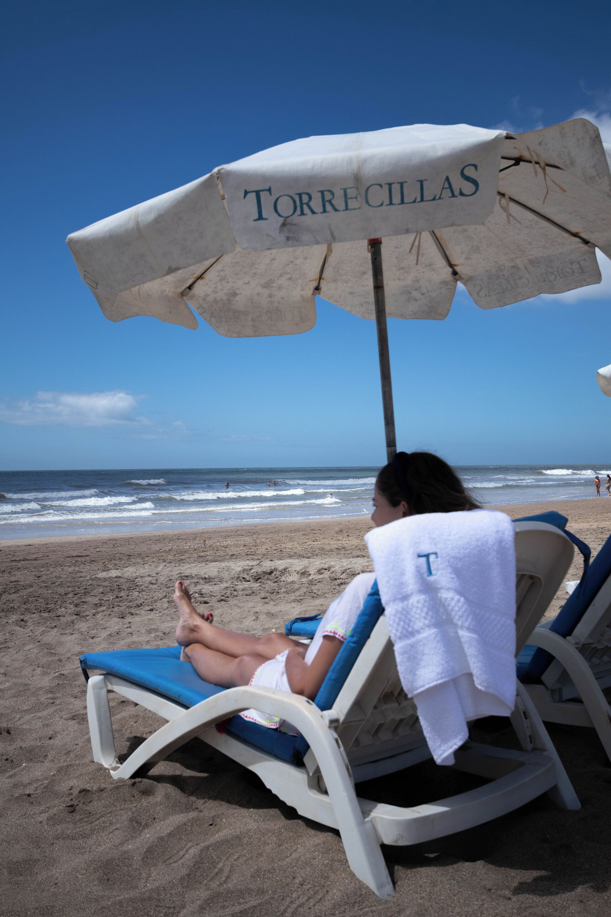 A beach scene with a person relaxing under a beach umbrella labeled "TORRECILLAS".