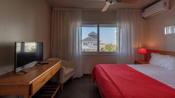 A hotel room with a bed, a desk with a TV, a chair, a window with curtains, and a ceiling fan.