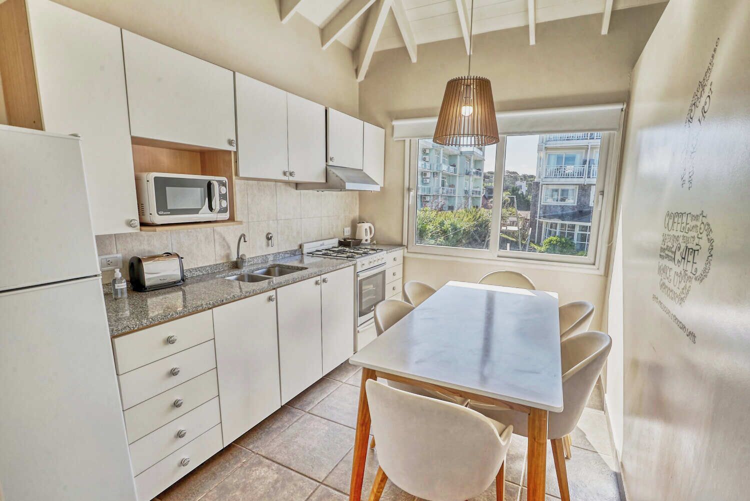 Une cuisine moderne avec des meubles blancs, un four à micro-ondes, une bouilloire et un coin repas comprenant une table et des chaises.