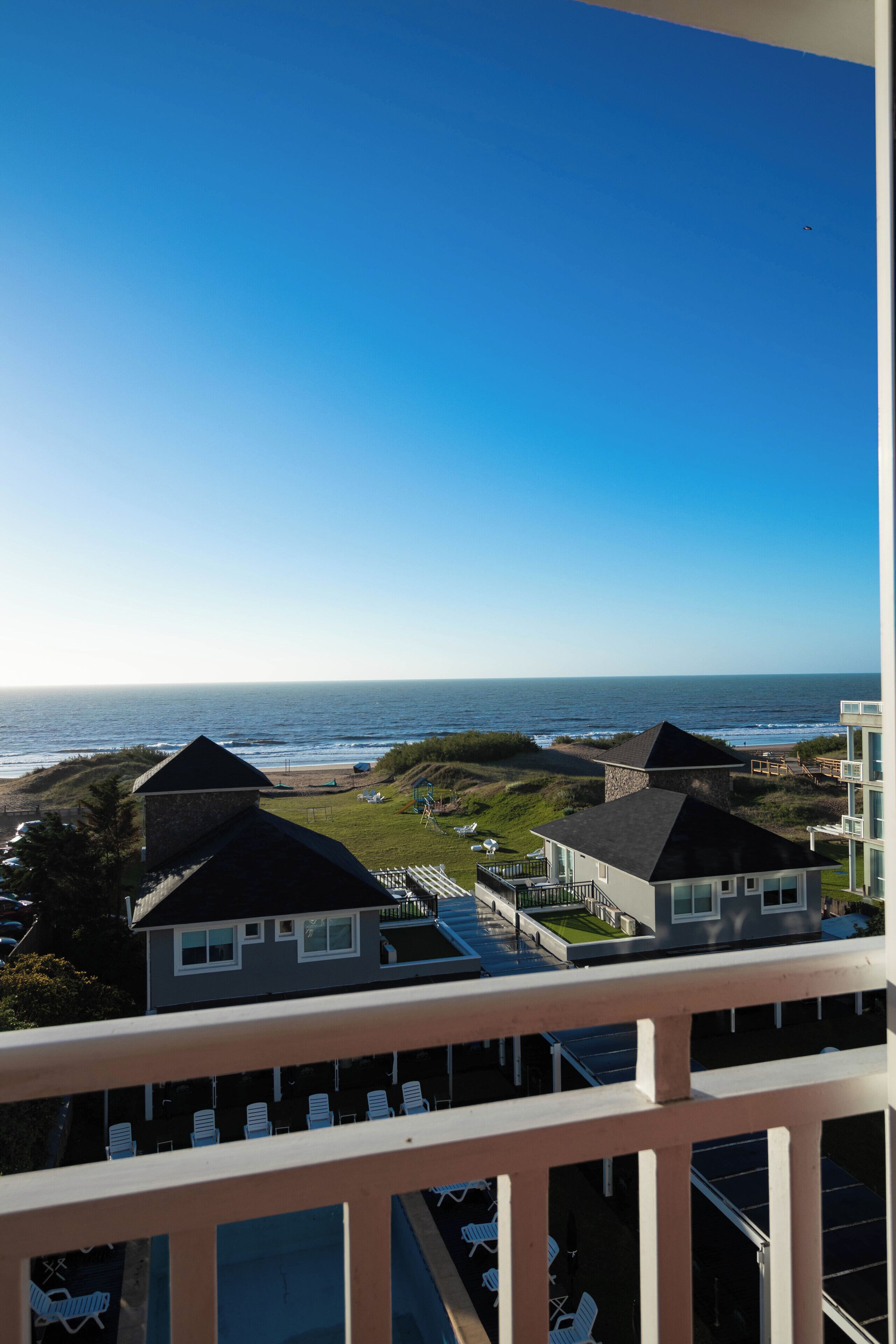 A coastal view from a balcony with a clear sky, a beach, and a building with a stone tower.