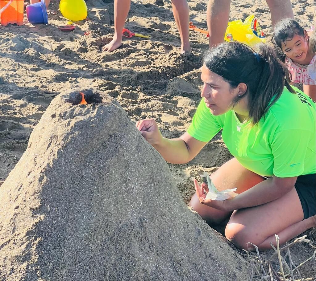 A person kneeling on a sandy beach, building a sandcastle.