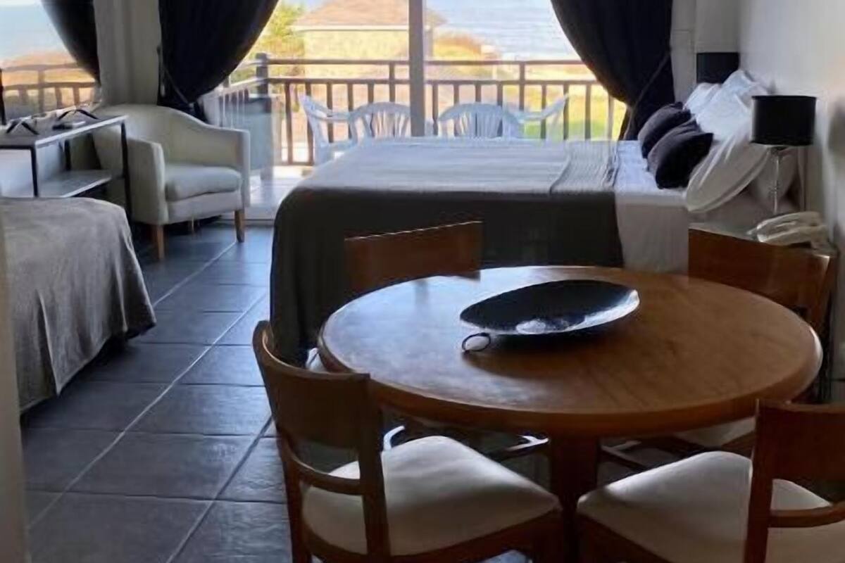 A room with a bed, a table with chairs, a small sofa, and a view of the sea.