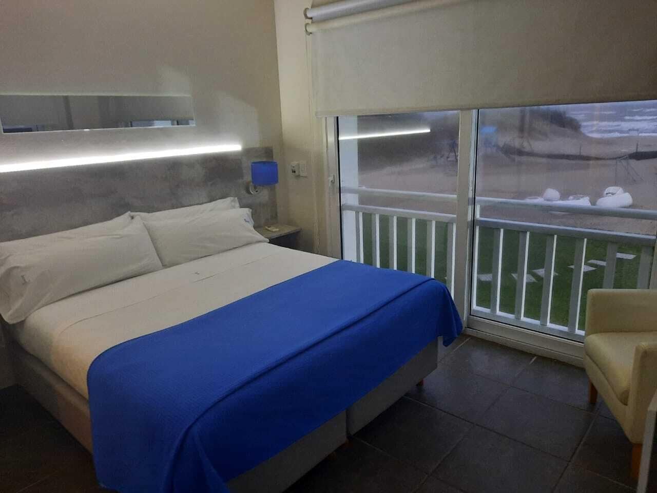 A hotel room with a bed, a nightstand, a blue bedspread, a chair, and a balcony with a railing.