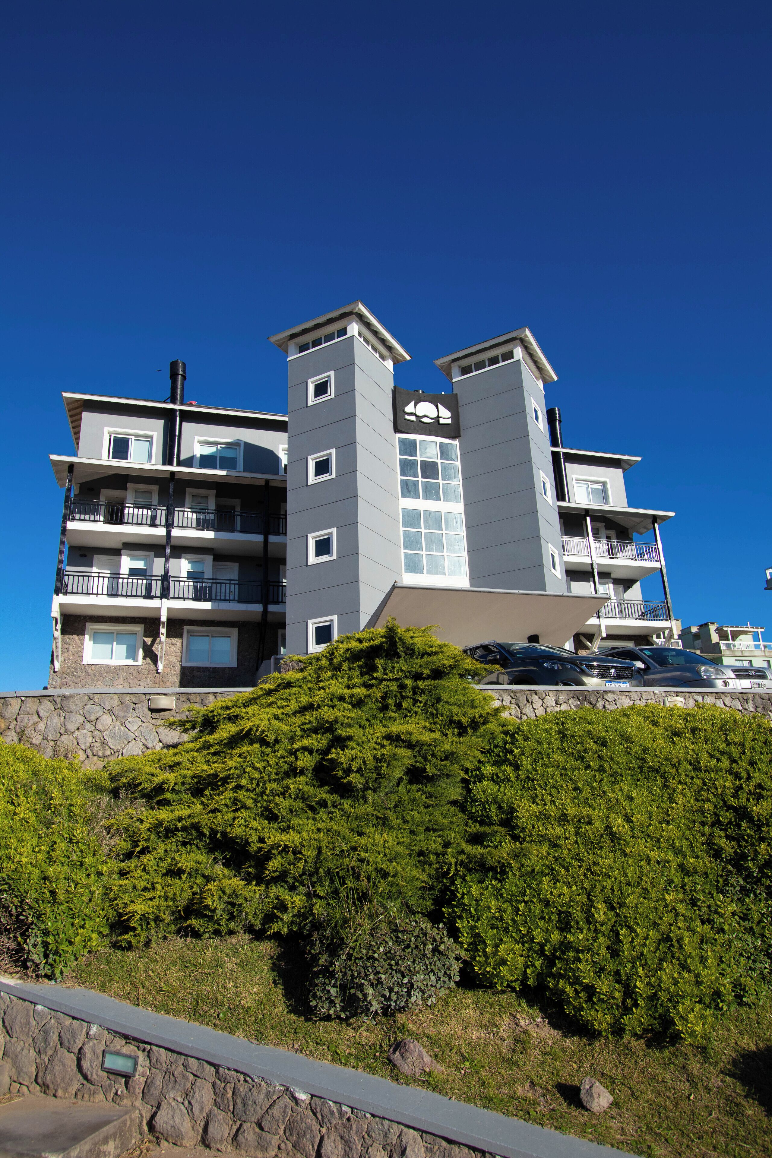 Un hôtel à plusieurs étages, doté de balcons, d’une façade en pierre et surplombant un ciel d’un bleu limpide.