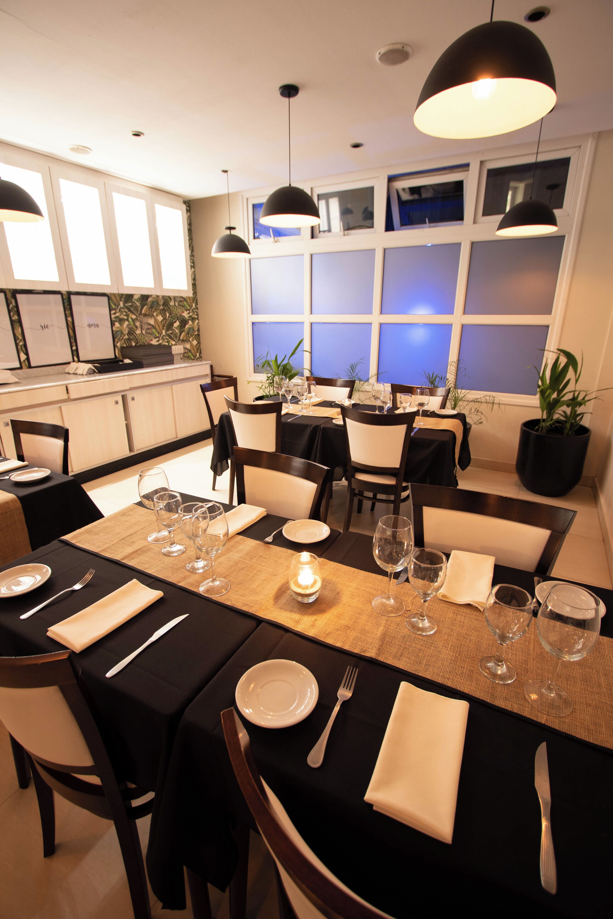 Een restaurant met gedekte tafels, zwarte tafelkleden, witte servetten en helder glazen bestek.