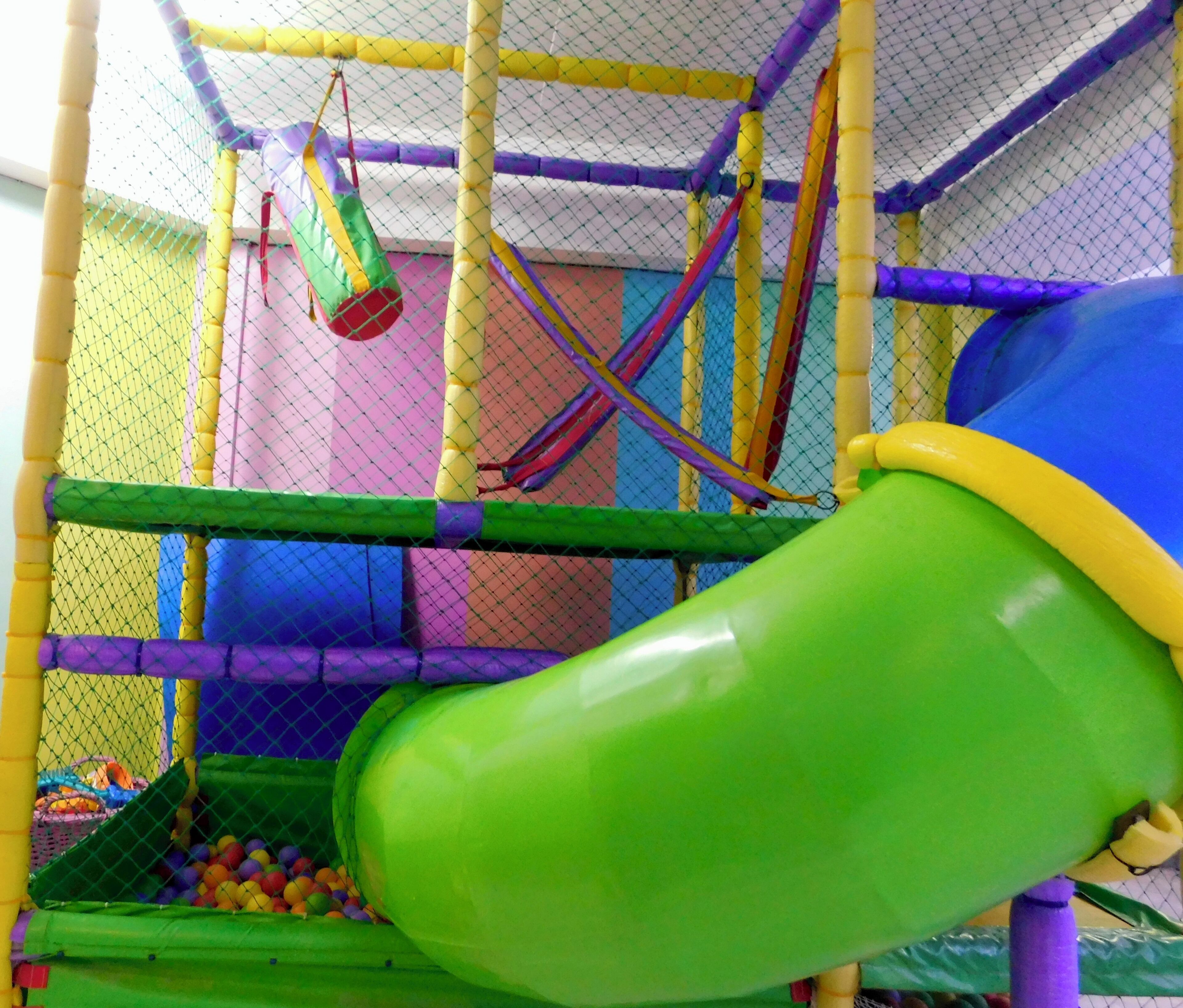 A colorful indoor play area with a slide, netted walls, and a ball pit.