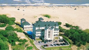 Une vue aérienne d’un grand hôtel composé de plusieurs bâtiments, avec une piscine et une plage en arrière-plan.