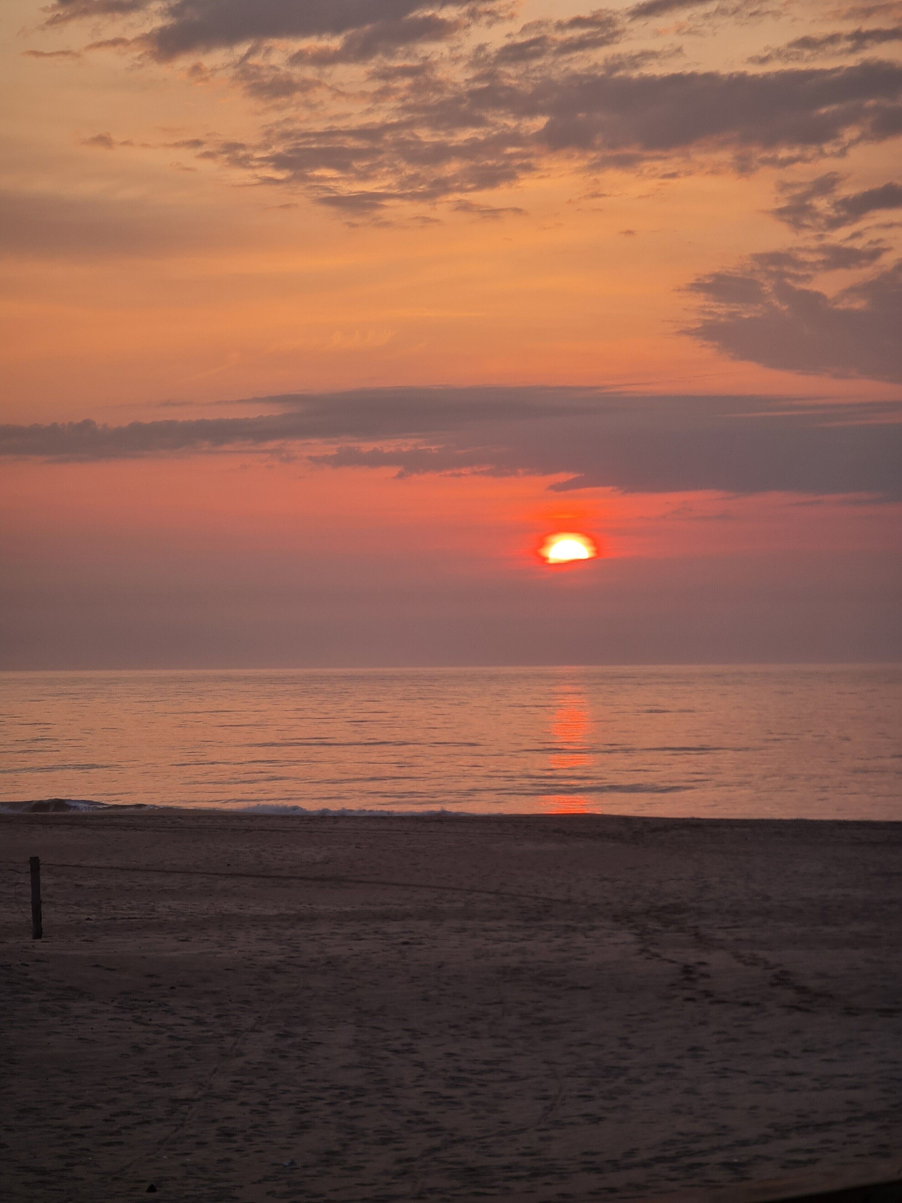 Un coucher de soleil sur une plage, avec une mer calme et un ciel dégagé.