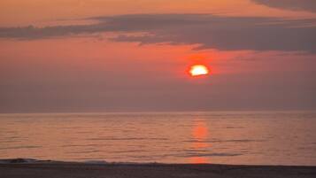 Un coucher de soleil sur une plage, avec une mer calme et un ciel dégagé.