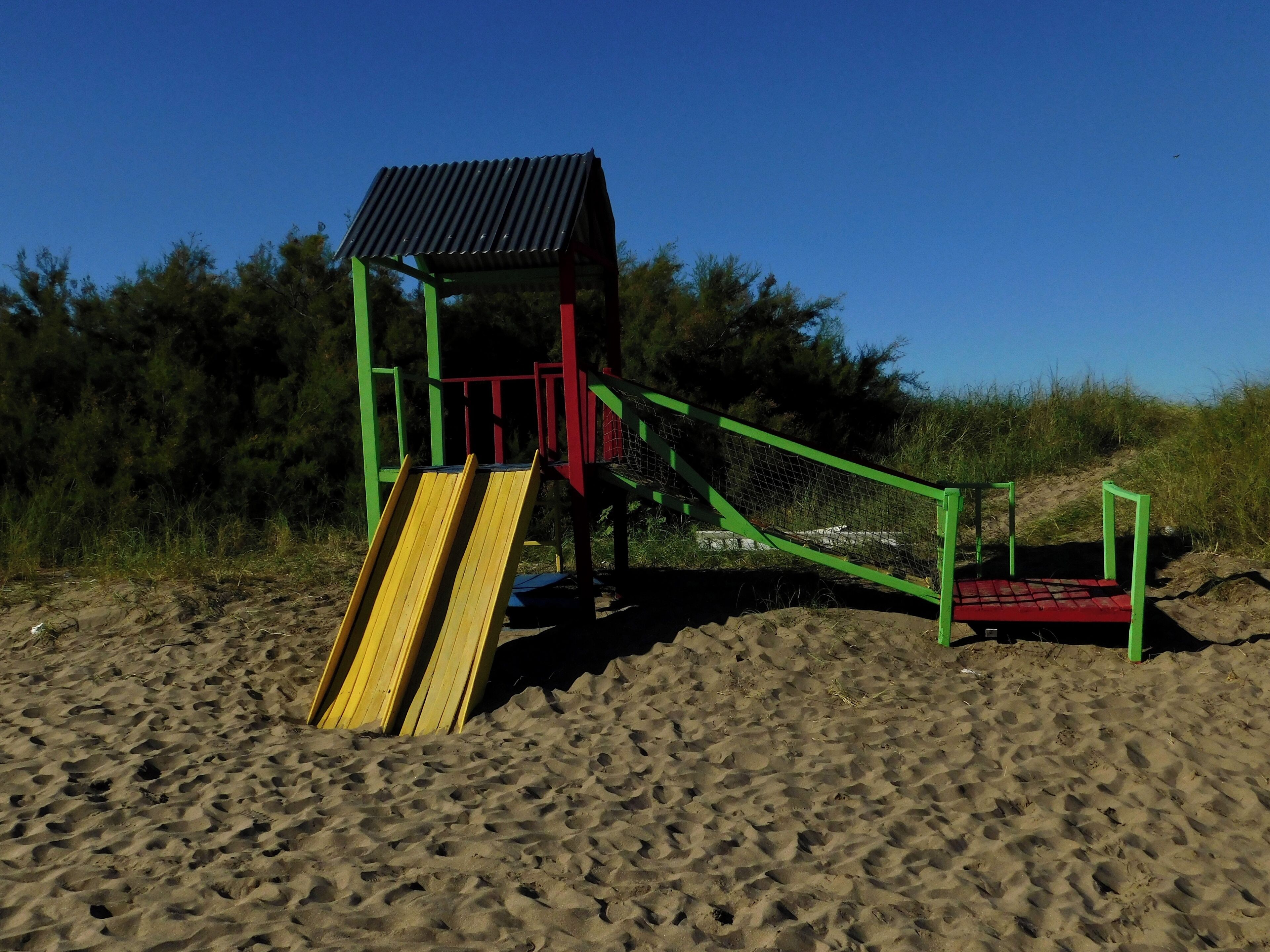 A playground with a slide and climbing structure on sandy ground.