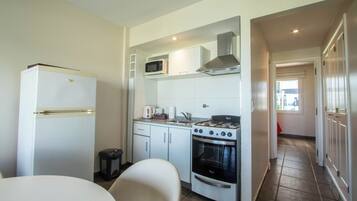 Cozinha compacta com geladeira, micro-ondas, fogão, forno e uma pequena área de jantar com mesa e cadeiras.