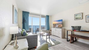Ein modernes Wohnzimmer mit einer Couch, einem Couchtisch und einem Essbereich mit einer Bank. Es gibt ein großes Fenster mit Vorhängen, ein Gemälde an der Wand und einen Laptop auf einem Schreibtisch.